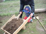 children and caretakers moving dirt with wooden wheelbarrow 